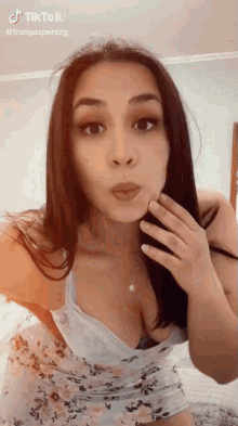 a woman in a floral dress is blowing a kiss while standing in front of a bed .
