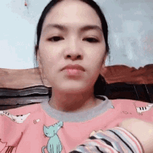 a woman is wearing a pink sweater with cats on it and making a funny face .
