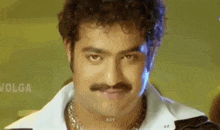 a man with curly hair and a mustache is wearing a white shirt and black jacket .