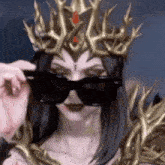 a woman wearing a crown and sunglasses is looking over her sunglasses .