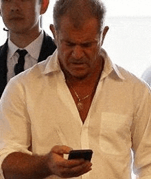 a man in a white shirt is holding a cell phone in his hand .