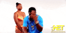 a man in a blue shirt is standing next to a woman in a bikini with a net logo behind them