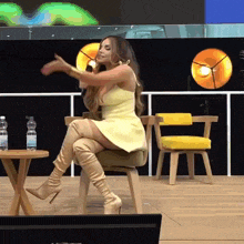 a woman in a yellow dress and over the knee boots sits on a chair