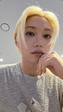 a woman with blonde hair is wearing a grey shirt and a necklace