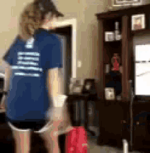 a woman in a blue shirt and shorts is standing in a living room in front of a television .