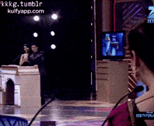 a woman sitting in front of a microphone with a screen behind her that says kkkg.tumblr