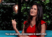 a woman in a red dress is sitting on a blue couch and pointing at another woman .