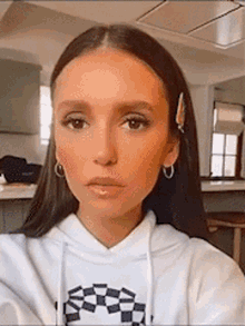 a woman is taking a selfie in a kitchen wearing a white hoodie and earrings .