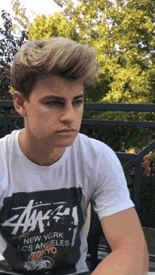 a young man wearing a white t-shirt that says new york los angeles and tokyo