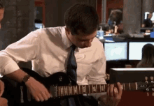 a man in a white shirt and blue tie is playing a guitar