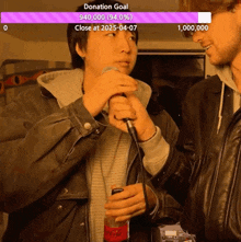 a man is holding a microphone in front of a donation goal
