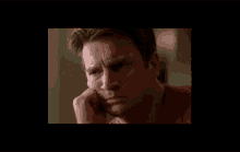 a man in a red shirt is talking on a cell phone with his hand on his chin .