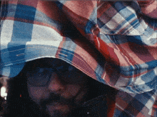a man wearing glasses and a plaid shirt is covering his head