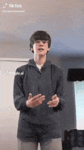 a young man wearing glasses and a grey hoodie is standing in a living room with his hands outstretched .