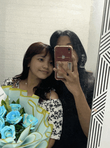 two girls are taking a picture of themselves in a mirror with a bouquet of blue roses in the foreground