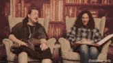 two men are sitting in chairs and one is reading a book and the other is laughing