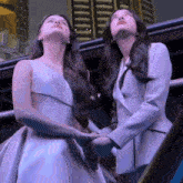 two women in white dresses are looking up at something