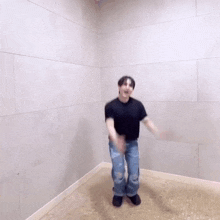 a man in a black shirt and jeans is dancing in a room with a white wall .