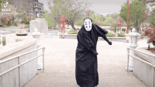 a person in a black costume with a mask on their face is dancing in a park with tik tok written on the bottom left