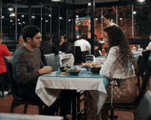 a man and a woman sit at a table in a restaurant talking to each other