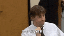 a man in a white shirt and tie is sitting at a table and talking to someone .