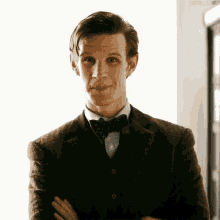 a man wearing a suit and bow tie is smiling with his arms crossed .