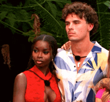 a man in a colorful shirt stands next to a woman in a red dress