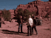 a group of men are standing in the desert with a car parked in the background