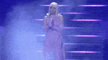 a woman in a pink dress and gloves is standing on a stage with her hands folded .