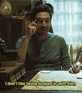 a man sitting at a table talking on a cell phone with the caption i don t like being lumped in