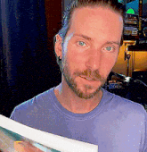 a man with a beard wearing a purple shirt is holding a book