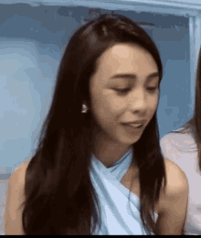 a woman with long hair is wearing a blue top and earrings and looking at the camera .