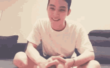 a young man in a white shirt is sitting on a couch with his legs crossed and smiling .