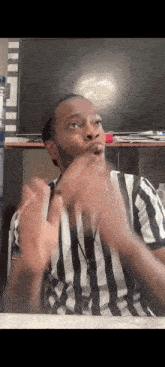 a man in a striped shirt is making a funny face while sitting in front of a television .