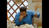 a man in a blue shirt is sitting at a table eating a meal .