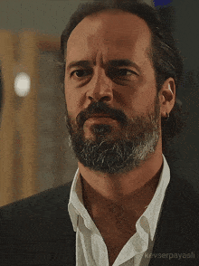 a man with a beard is wearing a black suit and white shirt with kayserpayasli written on the bottom
