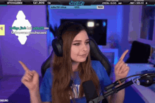 a woman wearing headphones and a blue shirt is sitting in front of a microphone and pointing