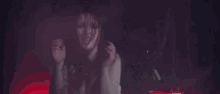 a woman with blood on her face is standing in front of a red car in a dark room .