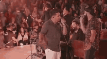 a group of men are singing into microphones on stage in front of a crowd .