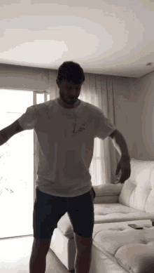 a man in a white t-shirt and blue shorts is standing in front of a white couch