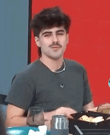a man with a mustache is sitting at a table eating food .