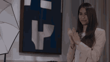 a woman applauds in front of a painting with the letter h on it
