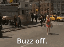 a woman in a trench coat is walking down a street with the words " buzz off " behind her