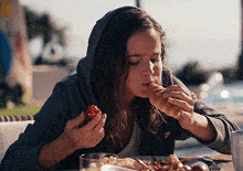 a woman wearing a nike jacket is eating a croissant