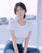 a woman wearing a white t-shirt and blue jeans is sitting on a window sill