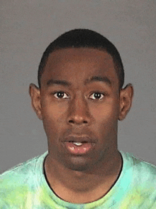 tyler the creator is wearing a tie dye t-shirt and making a funny face .