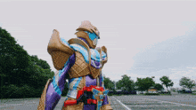 a purple and gold armored figure stands in a parking lot with trees in the background