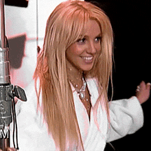 a blonde woman in a white robe is smiling in front of a microphone that has the letter m on it
