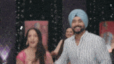 a man in a turban is dancing with a woman in a pink dress behind him .