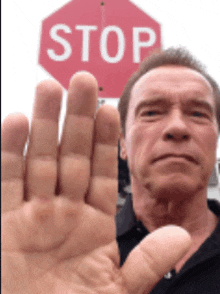 arnold schwarzenegger shows his hand in front of a stop sign